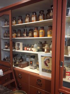 Museum recreation of Apothecary with small pill bottles in dark wood glass fronted cabinet.