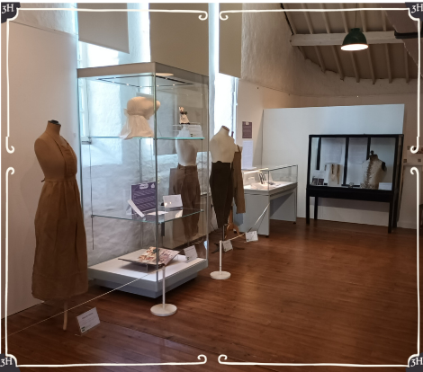 Photo of my Stories Told in Stitches at the Museum of Cornish Life. Cases can been seen displaying items relating to working women such as a balmaiden's cap. Also seen are mannequins wearing aprons and Women's Land Army uniforms