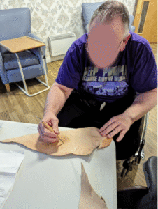 A man holds leatherworking stylus to carve a pattern into a piece of leather