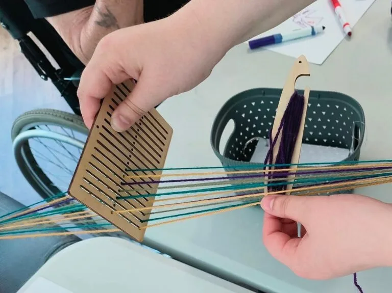 A heddleboard (a wooden board with small slots and holes) with thread in multicolours.