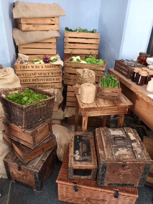 National Trust kitchen, crates of fake produce with text printed (as if the company of the crate) reading "This was a noisy busy place with daily deliveries of produce"